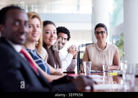 A diverse business team meets in a modern boardroom, collaborating around a conference table. Smiling professionals and a confident female leader convey teamwork, leadership, communication and positive corporate culture. Stock Photo