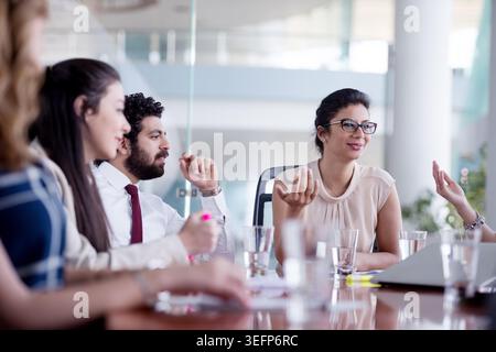 A diverse business team engages in a collaborative meeting in a modern office, sharing ideas, discussing strategy and planning projects around a glass conference table with laptops and notes. Stock Photo