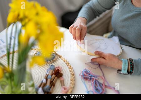 A woman creates an embroidery design using a pencil and colorful threads, surrounded by scissors and fabrics on a table Stock Photo