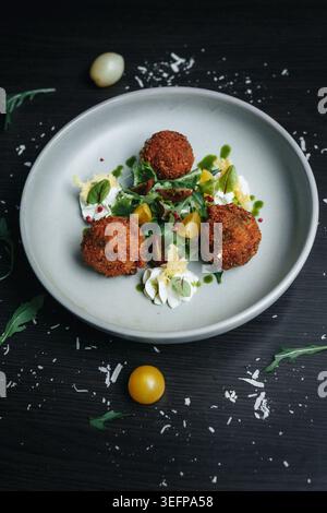 Croquettes with herb sauce and cherry tomatoes on dark table Stock Photo