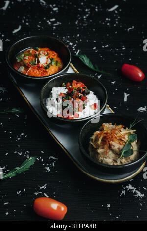 Three gourmet salads served in black bowls on a dark wooden tray Stock Photo