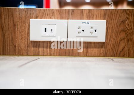 Close-up image of two electrical outlets mounted on a wooden wall near the floor, showing a power connection point with a clean and modern appearance. Stock Photo