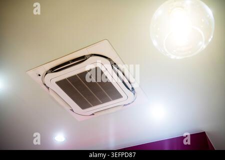 This image shows a modern ceiling-mounted air conditioning unit with integrated lighting, featuring sleek design and ventilation grille, common in con Stock Photo