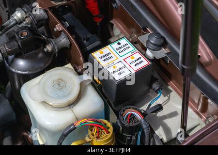 A close-up of a car engine bay shows a labelled relay box for screen wash, A/C clutch, cooling fan, and headlamp wash near the fluid reservoirs. Stock Photo
