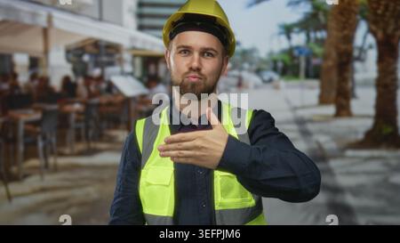 Man offering hand for handshake gesture on street outside restaurant terrace wearing helmet and reflective vest; trust reliability. Stock Photo