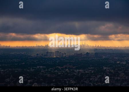 Panoramic view of New York City Manhattan skyline silhouette with golden sunbeams breaking through dark storm clouds at sunset Stock Photo