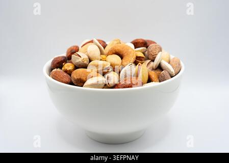 White bowl with mixed nuts isolated on white background. Healthy food concept with almonds, pistachios and natural protein snacks. Stock Photo