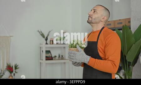 Man florist smelling a potted plant, nose close to tiny white flowers, holding wicker basket in a building; gentle care serenity. Stock Photo