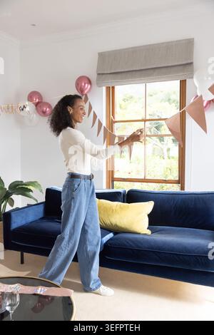 Triangular paper bunting is being attached across wooden-framed window, balloons clustering nearby Stock Photo