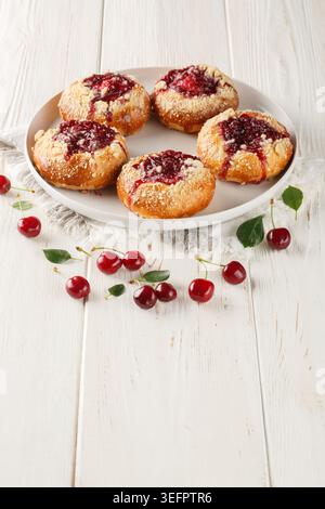 Sweet yeast buns with cherry filling and streusel close-up in a plate on a wooden table. Vertical Stock Photo