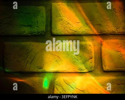 Yellow and green glowing reflections projected onto a textured brick wall. Abstract background with colorful illumination, rough masonry texture Stock Photo