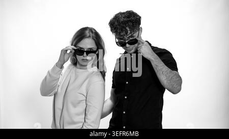 Young man and woman in sunglasses looking over their frames on a white studio background Stock Photo