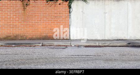 Boundary wall divided in two part, brick wall on the left and concrete on the left. Cement sidewalk and street in front. Background for copy space Stock Photo