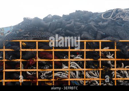 Industrial fishing nets in black and red piled inside a rusted yellow metal cage, conveying the scale and texture of commercial fishing equipment. Stock Photo