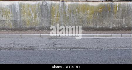 Grunge plaster wall peeled stained with mold and lichens. Sidewalk and street in front. Background for copy space. Stock Photo