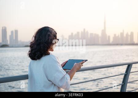 Remote worker using tablet outdoors with Dubai city skyline and waterfront view 4k video Stock Photo