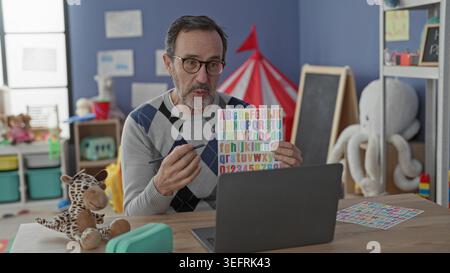 Man teacher holding colorful alphabet card and pointing with pencil at ...