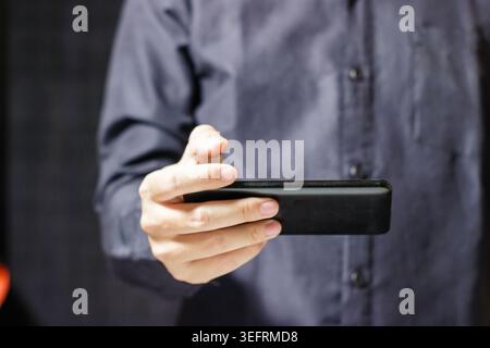 Man holding a black rectangular device in his hand. Playing a Video with Gadget. Business and Technology Concept. High quality photo Stock Photo