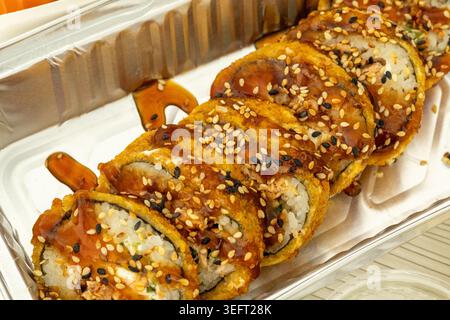 Crispy fried sushi rolls with sesame seeds and sweet soy sauce in a plastic takeout container Stock Photo