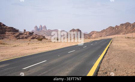 Asphalt road leading through empty desert landscape with sandstone mountains, Tabuk, Saudi Arabia Stock Photo
