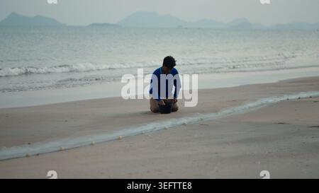 Fisherman kneeling separating catch from net on sandy beach at ao thung makham Stock Photo