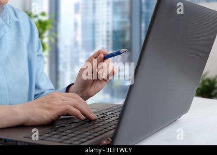 Closeup of woman using laptop and holding pen in modern office workspace, representing planning, online collaboration and business productivity workfl Stock Photo