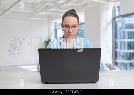 Focused businesswoman working on laptop in modern office interior, symbolizing concentration, remote work and digital productivity Stock Photo