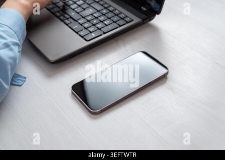Smartphone placed beside laptop on modern office desk, representing mobile communication, digital workflow and connected workspace Stock Photo