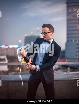 Elegant man celebrating success opening champagne on rooftop Stock Photo