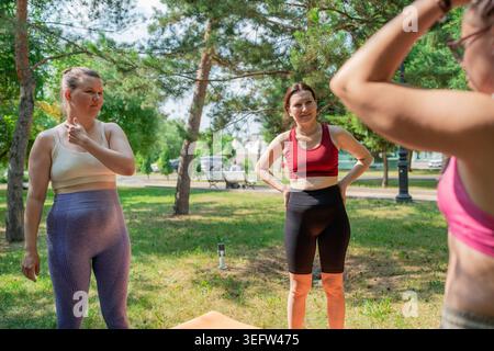 Women in sportswear talking and planning before group yoga session on mats in green park. Planning, yoga, talking, group, park, sportswear. Stock Photo