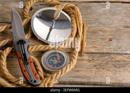 Top view survival gear set on rustic wooden background featuring pocket knife, rope, compass, and solar fire starter Stock Photo