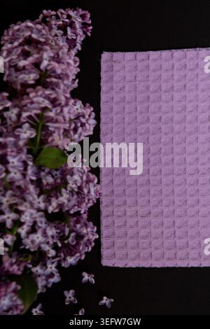 Purple fabric is placed next to fresh lilac flowers on a dark surface. This arrangement can be used for home decor or design projects. The combination Stock Photo