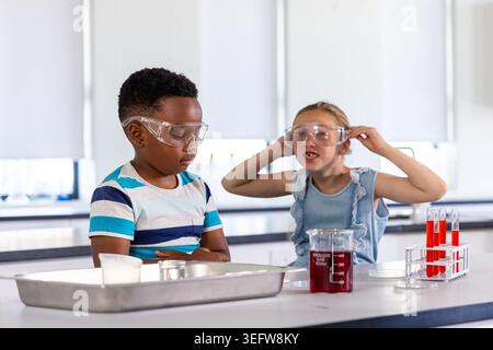 Diverse children doing experiment at school lab, wearing safety goggles, red beaker, test tubes Stock Photo