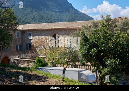 Historic stone estate building surrounded by olive trees and lush green vegetation in the Tramuntana mountains under a blue sky on a sunny day. Stock Photo