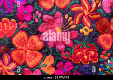 Close-up texture of colorful handmade floral embroidery on dark fabric. Stock Photo