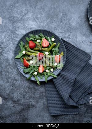 Top view of asparagus salad with strawberries mozzarella and greens on textured gray background Stock Photo