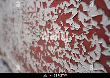 White paint peeling off a weathered red metal surface, creating a distinct texture. Stock Photo