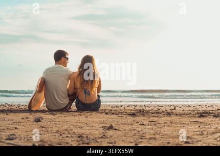 Unrecognizable pair captured from behind in a candid and genuine moment, with the sound of the sea and warm afternoon light setting a relaxed and care Stock Photo