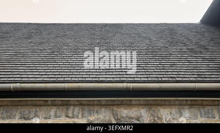 old teak wood shingle roof over rough stone block wall in straight view, wooden part of ancient architectural residential building Stock Photo