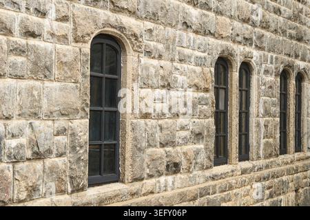 black arched old windows on long grey stone wall, building facade with uneven chiseled blocks, side angle view, ancient architecture concept Stock Photo