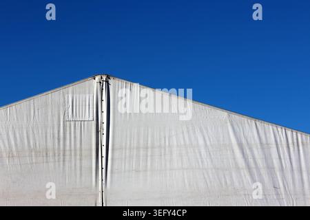 Triangular roofline of a white commercial marquee tent against a clear, deep blue sky Stock Photo