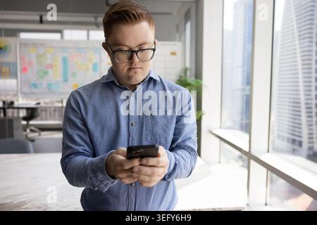 Serious man with Down syndrome using smartphone during work break Stock Photo