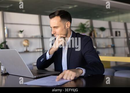 Focused businessman reviewing printed charts thoughtfully at office desk Stock Photo