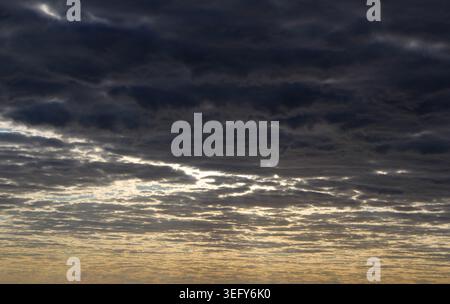 Dramatic dark storm clouds layered over a bright golden sunrise sky Stock Photo