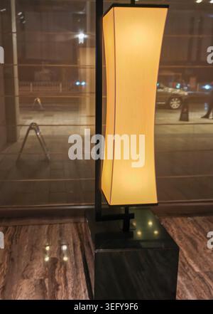 Modern floor lamp with a curved shade illuminated in a stylish interior setting, showcasing a sleek black base and warm light against a marble floor Stock Photo