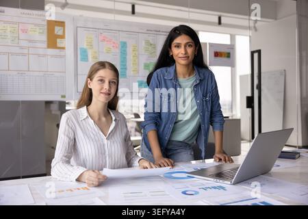 Two smiling multiethnic women teammates looking at camera during teamwork Stock Photo