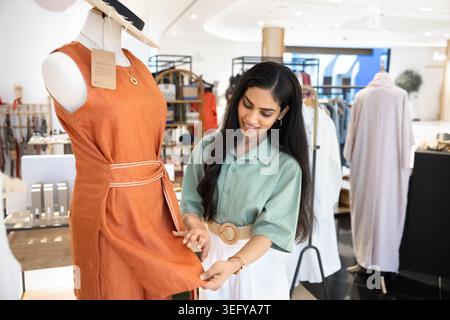 Woman inspecting dress displayed on mannequin in modern clothing boutique Stock Photo