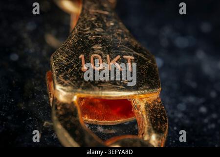 Extreme macro close up of a shiny ten karat yellow gold jewelry clasp engraved with 10KT purity stamp isolated on a dark speckled background Stock Photo