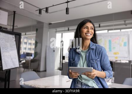 Positive businesswoman looks into distance with thoughtful and dreamy expression Stock Photo