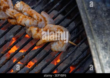 Wooden skewer packed with seasoned raw shrimp cooking on a metal grill Stock Photo